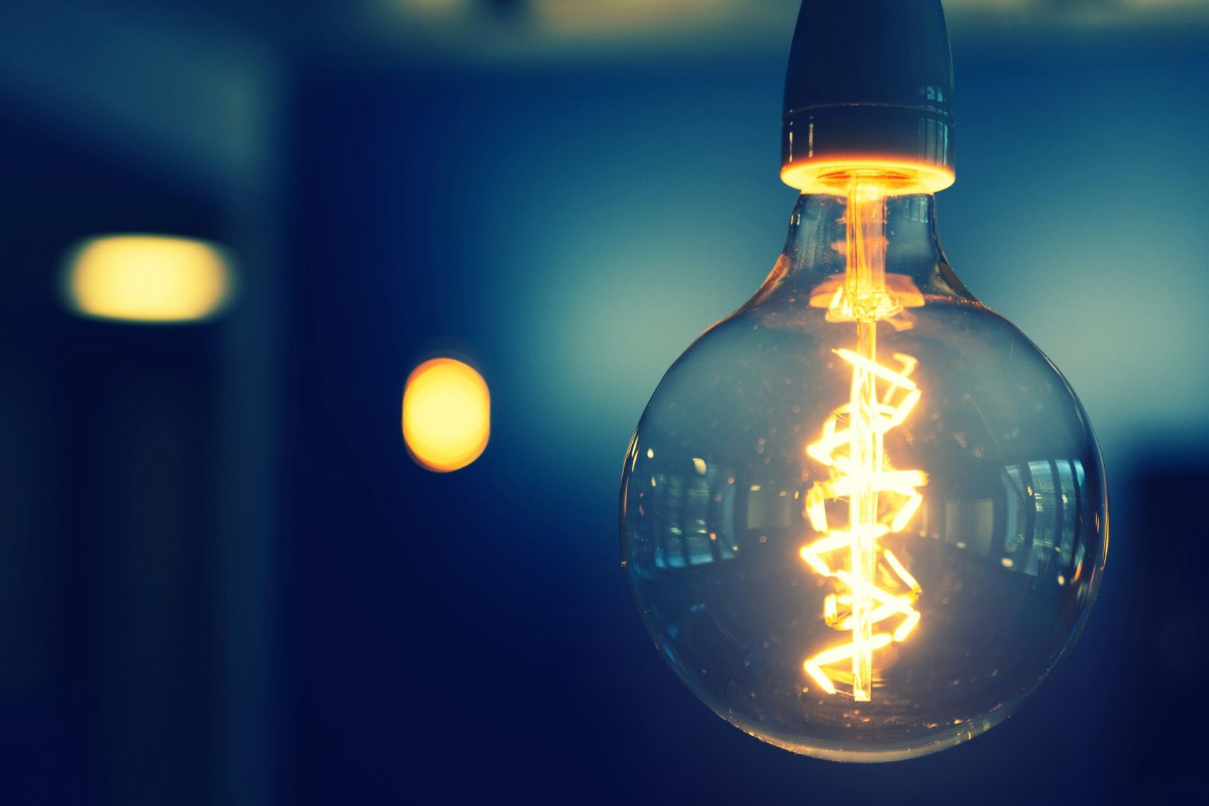 A filament light bulb glowing against a dark blue background