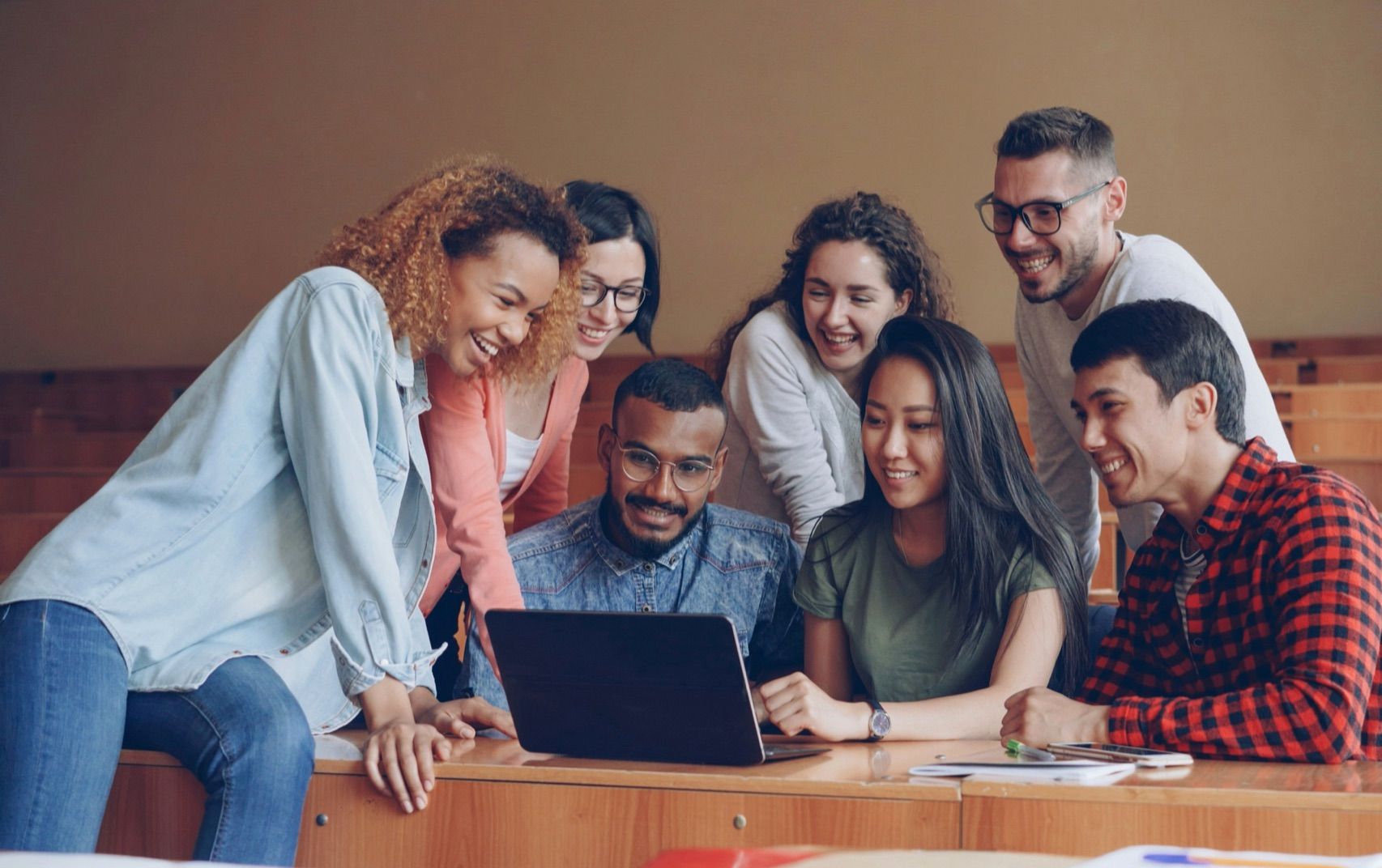 Six colleagues gathered around a laptop, smiling as they work together