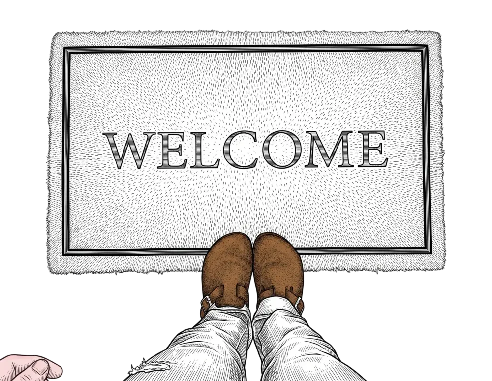 Looking down at a pair of feet in brown shoes standing on a doormat that reads WELCOME