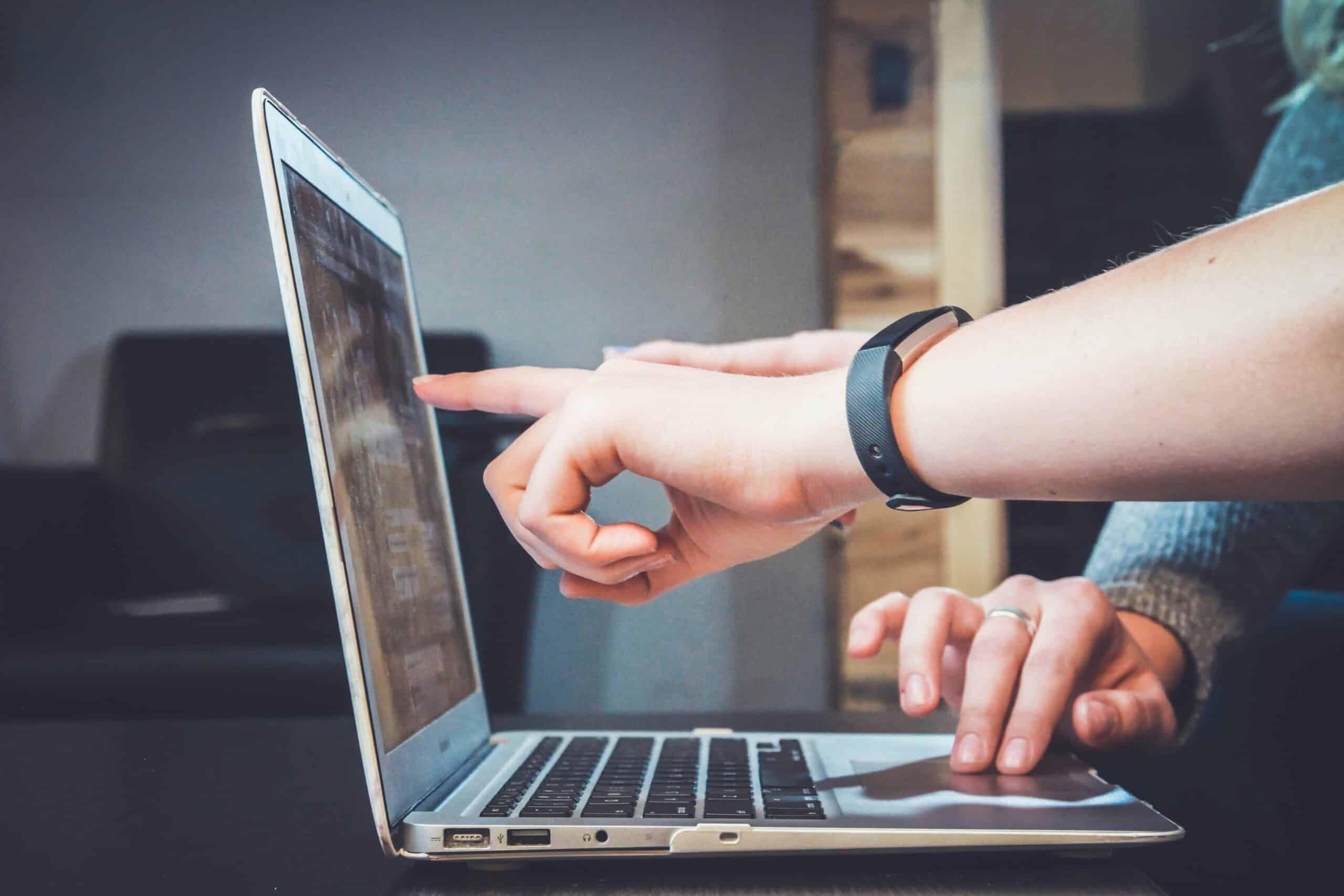 Two people are looking at a laptop screen and pointing at it.