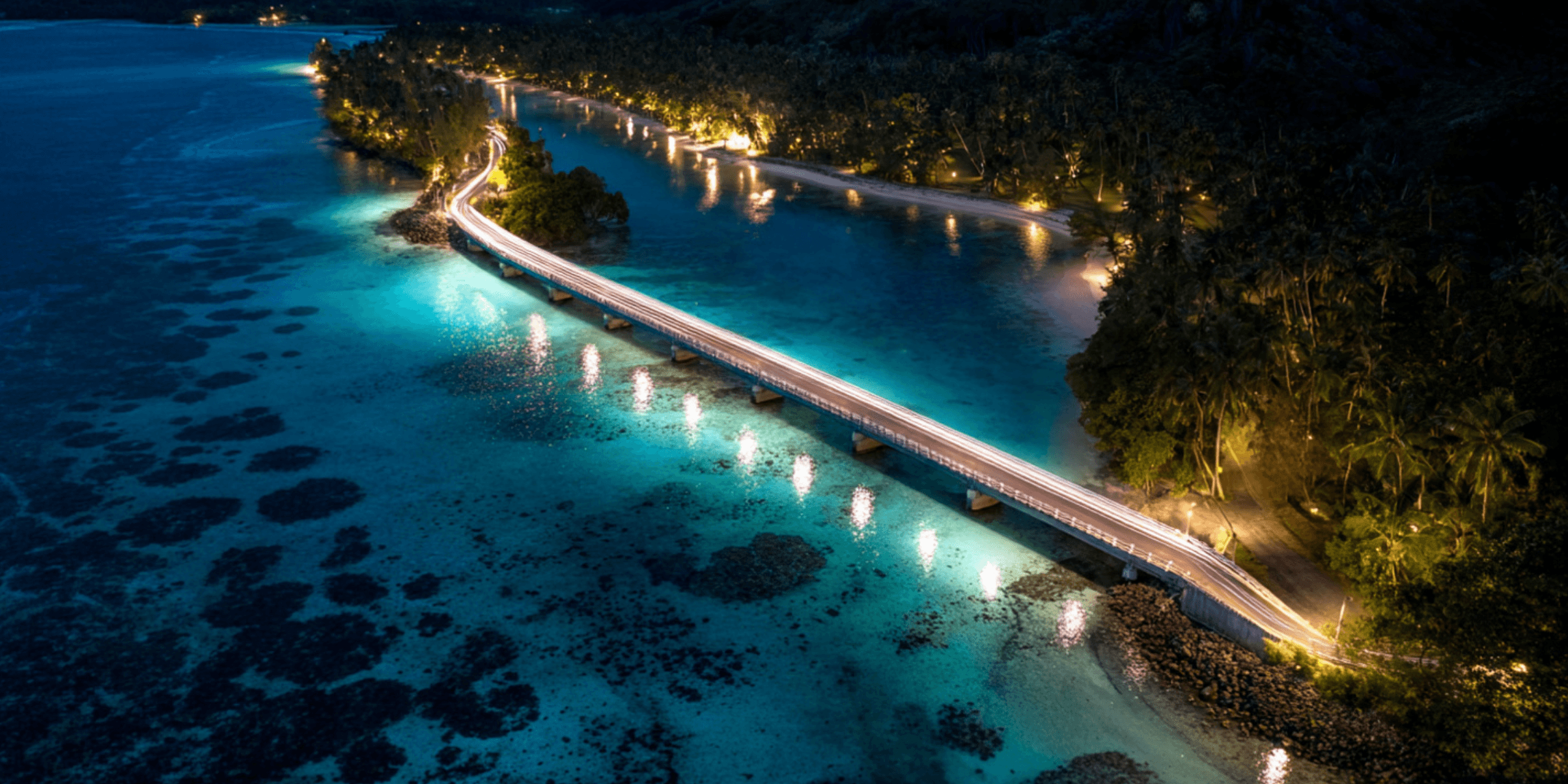 A beautifully lit bridge connecting two islands in the South Pacific at night.